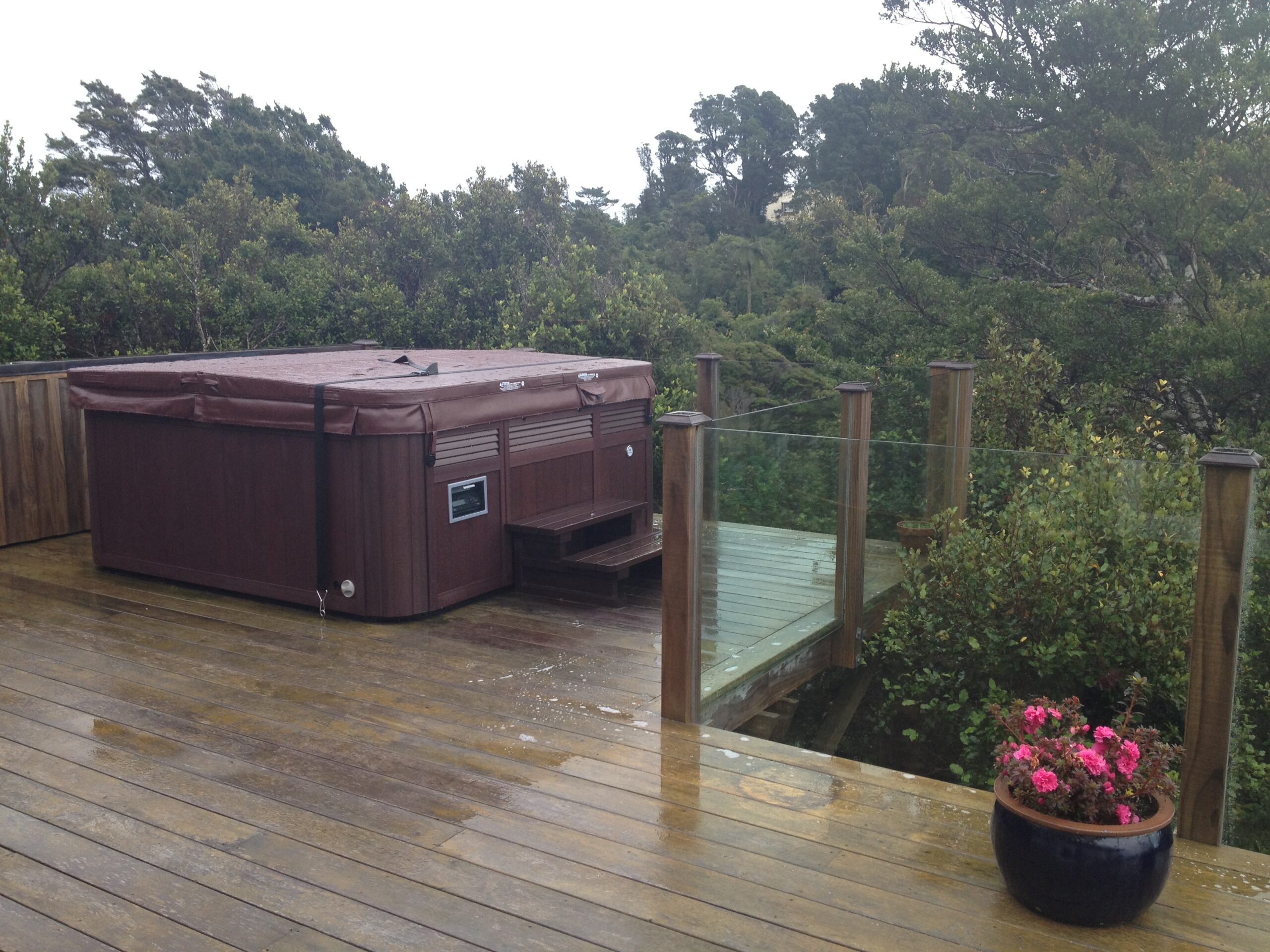 Spa with wind straps on a wet timber deck beside a glass fence