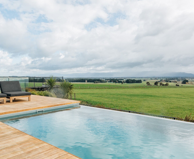 Infinity pool fencing beside a rectangular pool with timber decking and open rural views