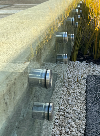 Glass swimming pool fencing fixed to a concrete edge with metal mounts
