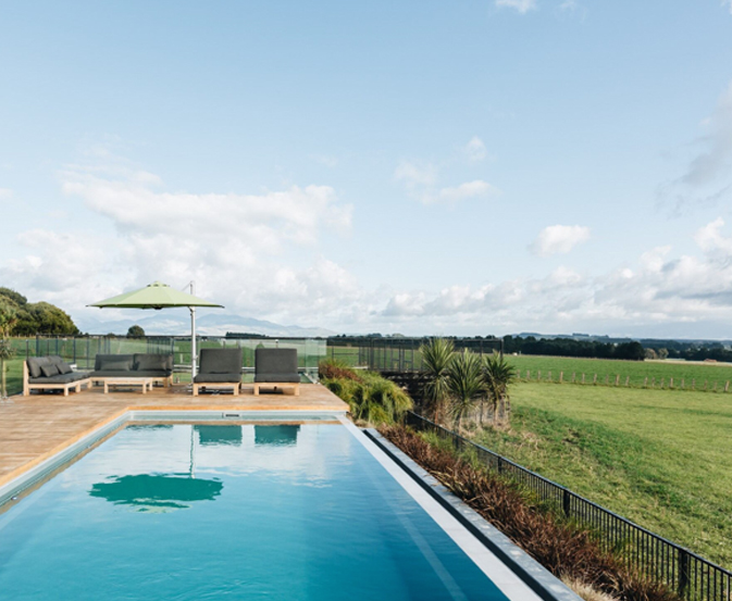 Infinity pool fencing beside a long pool with rural views and outdoor seating