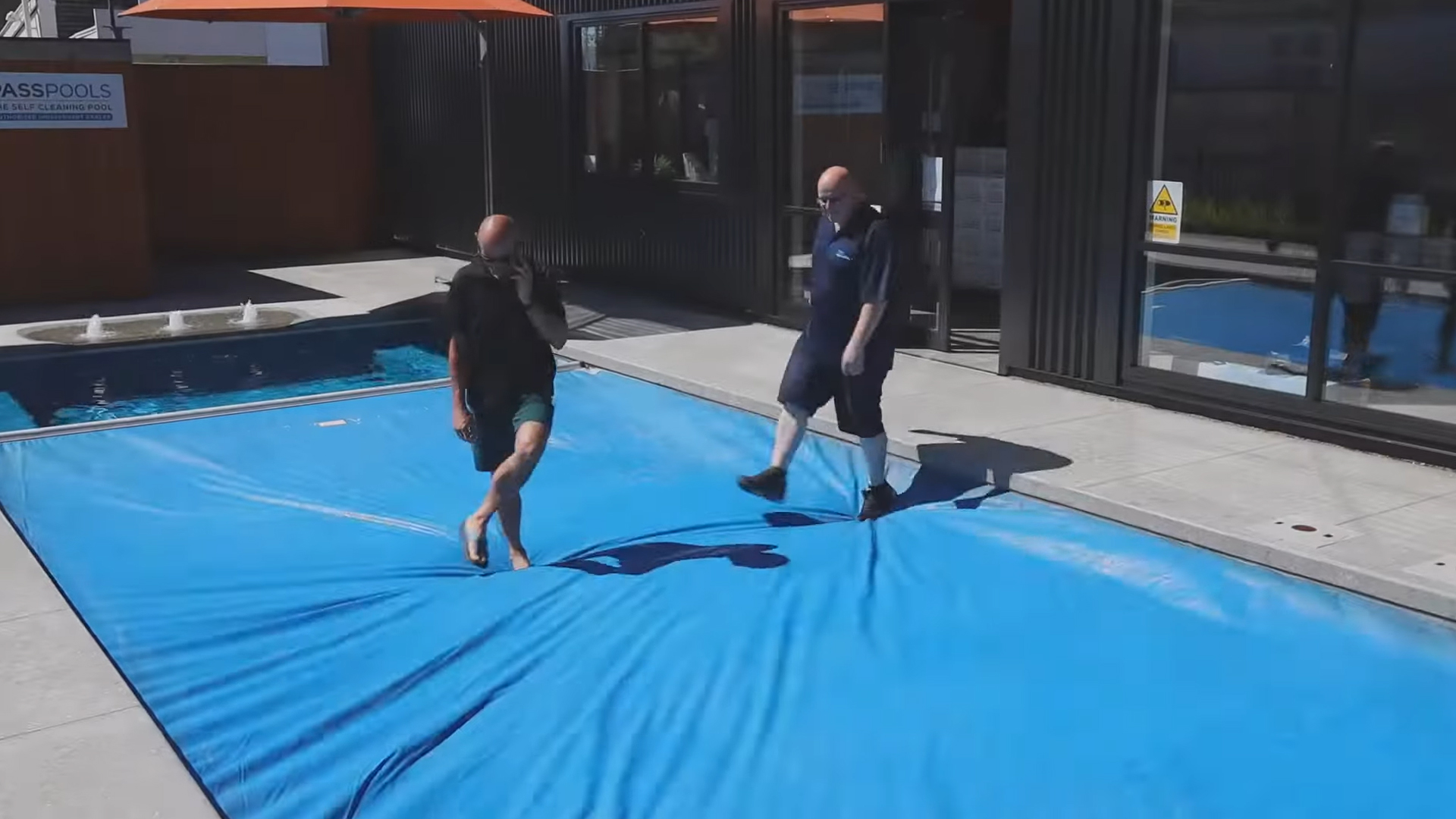 Two adults standing on an automatic sealing pool cover fitted to a swimming pool, demonstrating the safety and durability of the cover system when closed.