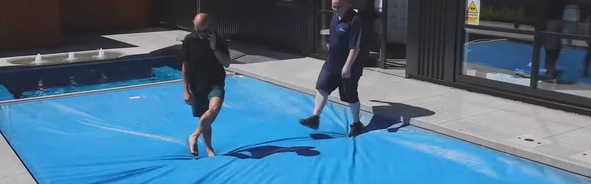 Two adults standing on an automatic sealing pool cover fitted to a swimming pool, demonstrating the safety and durability of the cover system when closed.